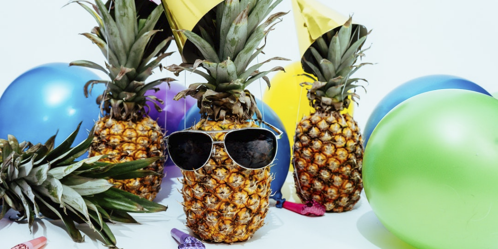 This image is of three pineapples wearing sunglasses with balloons around them 